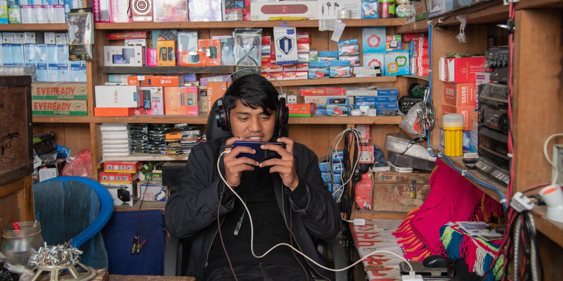 Person working in an electronics shop, wearing headphones and watching his phone.